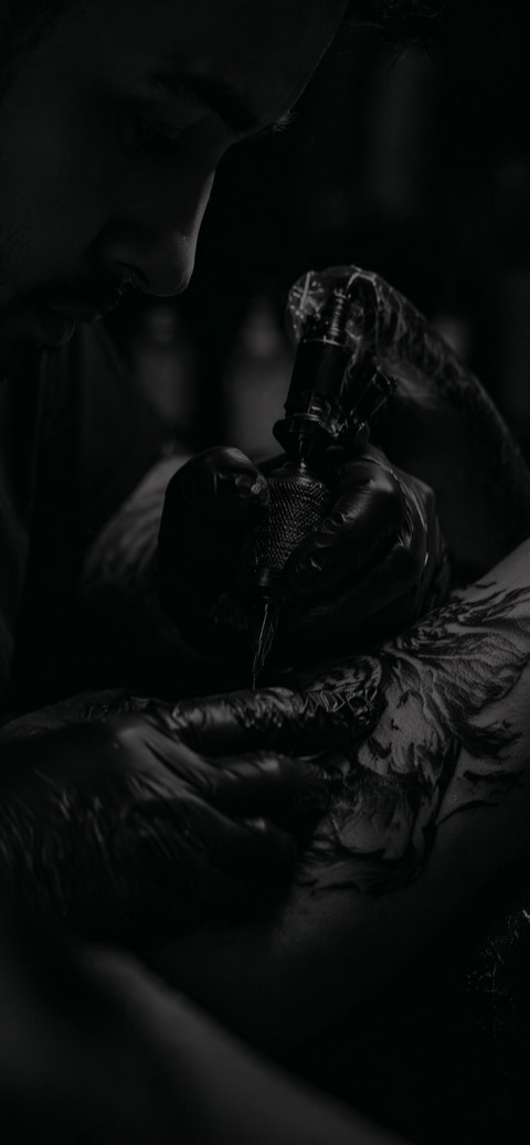 Tätowierer arbeitet konzentriert an einem Black-and-Grey-Tattoo bei gedämpftem Licht